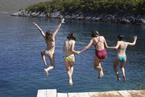 Cuatro adolescentes saltando desde el muelle en agua de mar - foto de stock