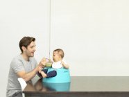 Pai alimentando bebê menino no assento do bebê — Fotografia de Stock