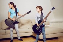 Мальчик и девочка в гостиной играют на гитаре, отводя взгляд — стоковое фото