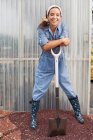 Young woman in dungarees leaning on spade in garden centre, portrait — Stock Photo