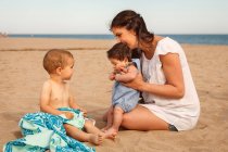 Madre e bambini seduti sulla spiaggia — Foto stock