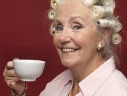 Portrait studio de femme âgée en rouleaux de cheveux avec tasse de thé — Photo de stock