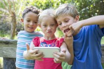 Троє дітей беруть селфі на смартфон в саду — стокове фото