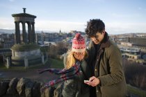 A young couple photograph themselves on Calton Hill with the background of the city of Edinburgh, capital of Scotland — Stock Photo