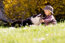 Baby girl playing with dog in grass — Stock Photo