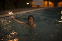 Boy in swimming pool playing with sparkler on 4th July — Stock Photo