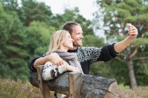 Mid adult couple on bench photographing themselves — Stock Photo