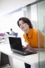 Trabajadora de oficina usando laptop, inclinada hacia adelante - foto de stock