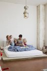 Сім'я з трьома доньками, які читають книжки в ліжку — стокове фото