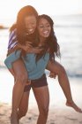 Woman carrying friend on beach — Stock Photo