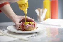 Женщина, брызгающая пончиком с кетчупом и горчицей — стоковое фото
