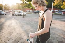Молодий чоловік міський скейтбордист слухає музику навушників на тротуарі — стокове фото