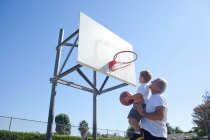 Hombre levantando nieto a aro de baloncesto - foto de stock