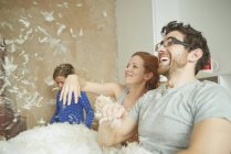 Mid adult couple pillow fighting daughter in bed — Stock Photo