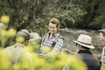 Small group of people by river with fishing rod smiling — Stock Photo