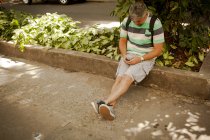 Mature man sitting on sidewalk texting on smartphone, Rio De Janeiro, Brazil — Stock Photo