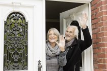 Senior couple waving by front door — Stock Photo