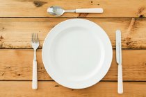 Empty plate with cutlery on wooden table, top view — Stock Photo