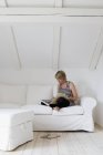 Mujer madura sentada con las piernas cruzadas en el sofá libro de lectura - foto de stock