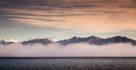 Misty seashore and mountains under cloudy sunset sky — Stock Photo
