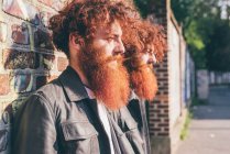 Young male hipster twins with red hair and beards leaning against brick wall — Stock Photo