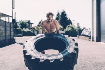 Young male cross trainer lifting heavy tyre outside gym — Stock Photo
