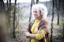 Mature woman standing in woodland with arms folded — Stock Photo