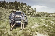 Retrato del hombre y el hijo adolescente en un viaje de senderismo por carretera apoyado en la capucha del automóvil en el paisaje, Bridger, Montana, Estados Unidos - foto de stock