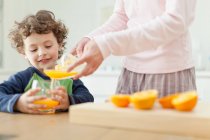 Mother pouring orange juice for son, cropped view — Stock Photo