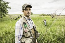 Homme dans le champ tenant canne à pêche regardant caméra — Photo de stock