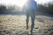 Rear view of runner running on frosty grass — Stock Photo
