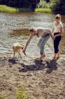 Casal brincando com cão na beira do rio — Fotografia de Stock