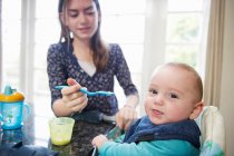 Girl feeding baby brother at table — Stock Photo