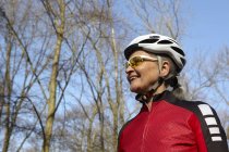 Низький кут зору жінки в велосипедному шоломі і сонцезахисних окулярах дивиться геть посміхаючись — стокове фото