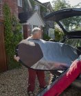 Senior man loading surfboard into car boot — Stock Photo