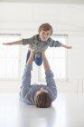 Father lying on floor holding up son — Stock Photo
