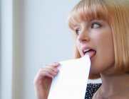 Portrait of woman with blonde bob licking envelope — Stock Photo
