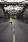 Rear view of young male athlete running over bridge — Stock Photo