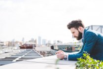 Молодий бізнесмен читає текст смартфона на терасі на даху офісу — стокове фото
