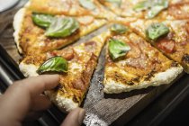 Hand nimmt ein Stück Pizza mit Basilikum — Stockfoto