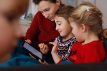 Mãe e filhas no sofá sentado usando tablet digital sorrindo — Fotografia de Stock