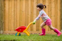 Молодая девушка бежит с игрушечной тачкой в саду — стоковое фото