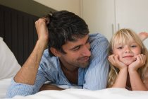 Padre e hija acostados en una cama - foto de stock