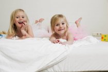 Retrato de dos hermanas preescolares acostadas en la cama - foto de stock