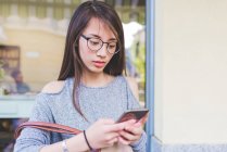 Молода жінка смс на смартфоні за межами тротуарного кафе — стокове фото