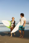 Couple marchant sur la plage, portant des planches de surf — Photo de stock