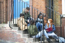 Jóvenes estudiantes universitarios adultos charlando y revisando en las escaleras del campus - foto de stock