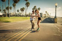 Young woman on skateboard at San Diego beach, boyfriend helping — Stock Photo