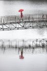 Young woman in red crossing footbridge in rain — Stock Photo