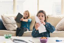 Girls at home using digital tablet, making paper airplane — Stock Photo